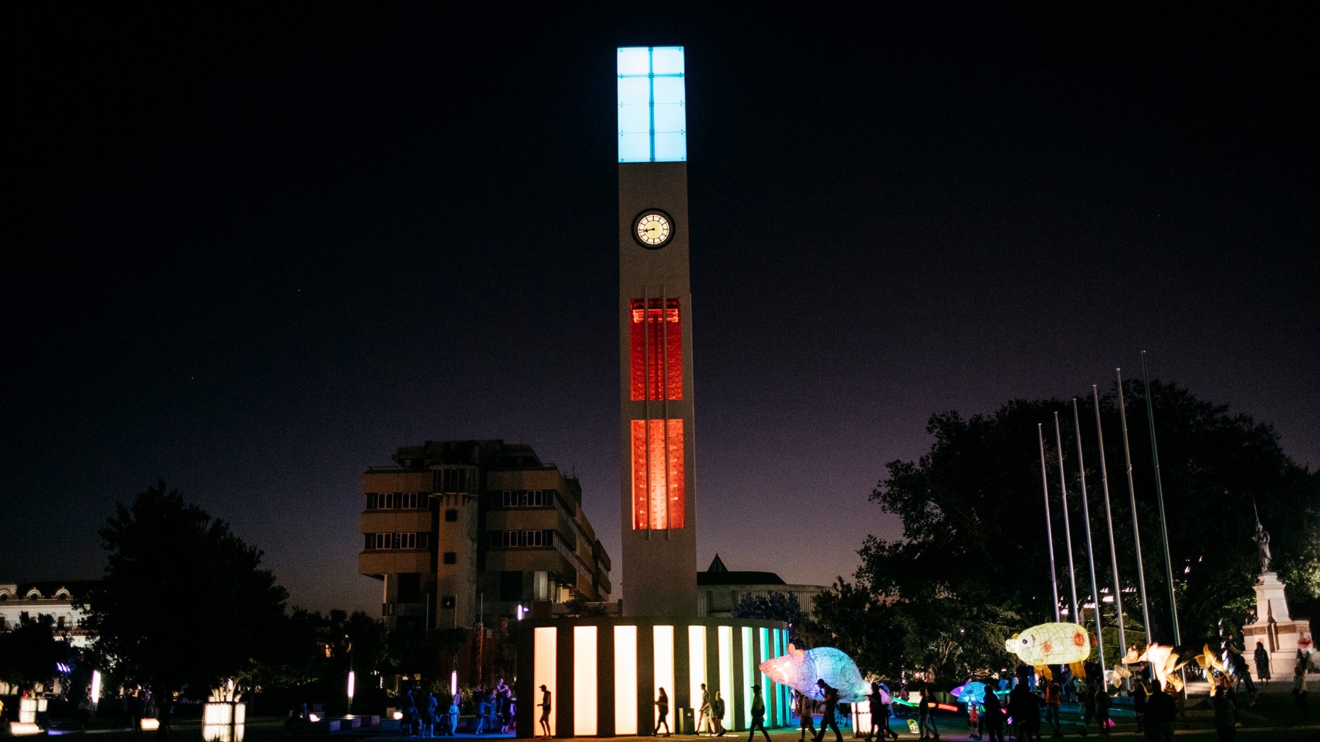 Image shows the clock tower lighting red and blue in early evening
