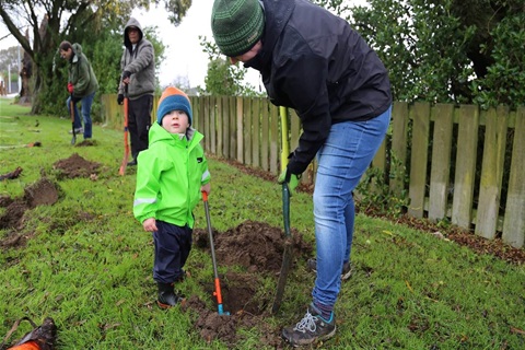 Toddler and his caregiver digging a hole to plant a tree with other people digging in the background.