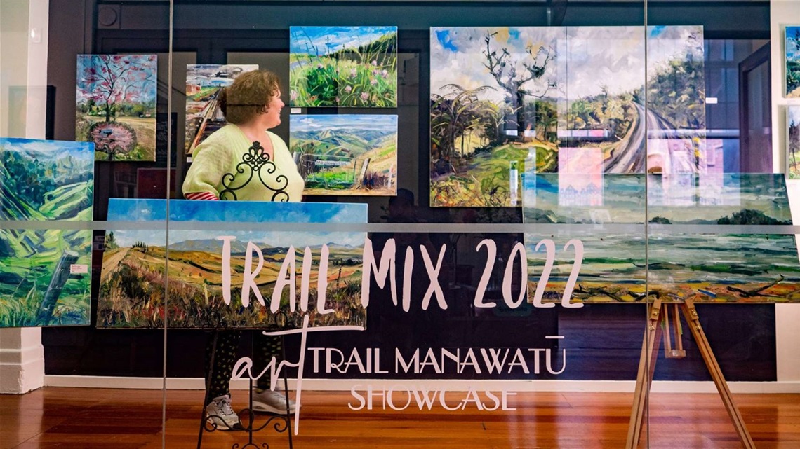 A woman spotted through an art gallery window, looking at paintings exhibited on the wall inside.