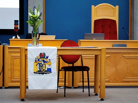 Picture shows a set of table and chair in the council chamber, with a flag of Palmerston North on the table