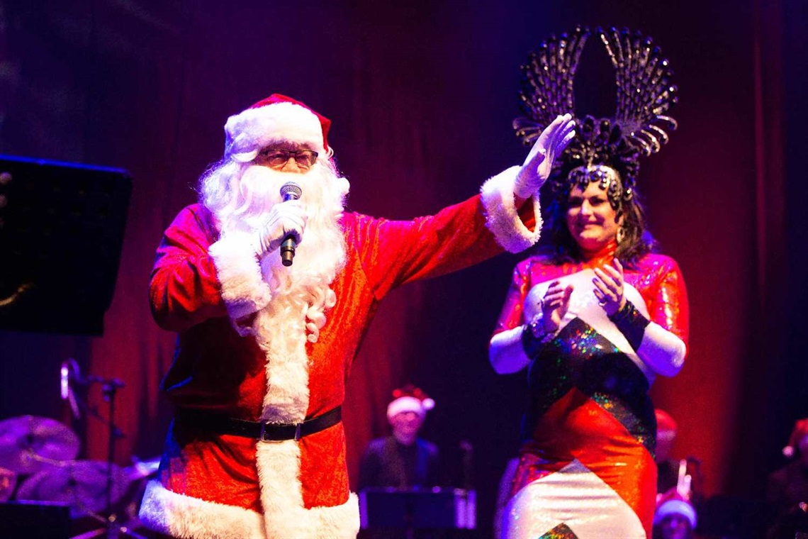 Photo shows a man wearing Santa suites speaking on stage