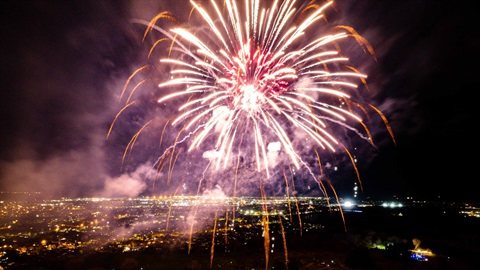 Photo shows aerial view of fireworks lighting up the night sky, with the city as background