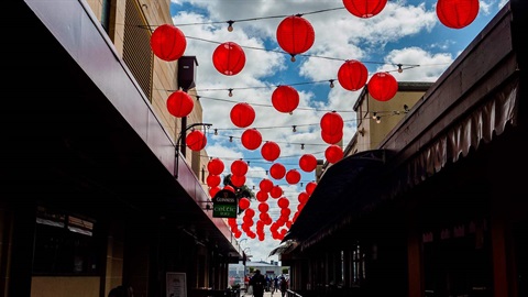 Image shows a lot of red lanterns hanging over a narrow street
