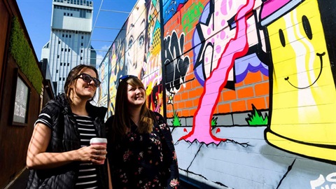 Two young women stroll through a laneway looking at the murals.