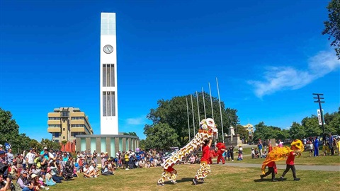 Photo shows the crowd watching lion dance under the white clock tower. 