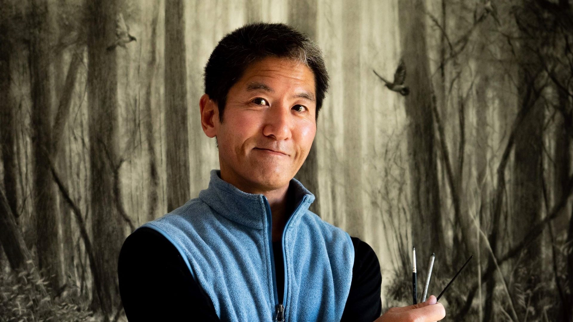 Palmy artist Naga Tsutsumi standing in front of one of his large-scale works, brushes in hand.