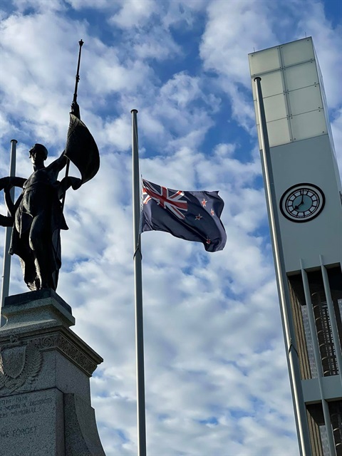 Photo shows the New Zealand national flag half-masting beside a clock tower