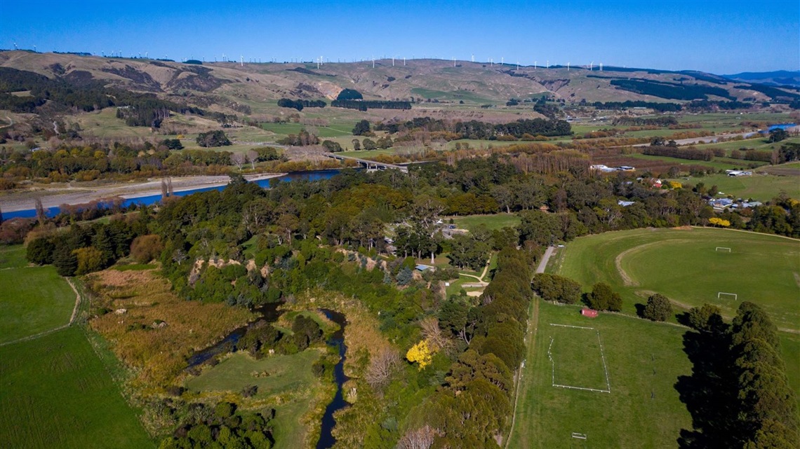 Photo shows aerial shot of Ashhurst Domain including the pony club grounds, with lots of trees and the river and hills in the background.