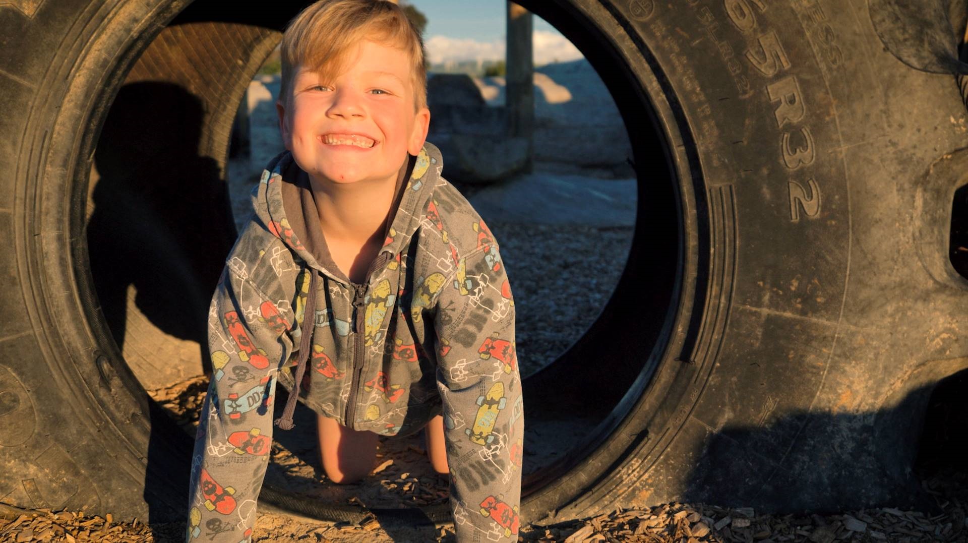 Grinning boy crawls through a tyre in the playground.