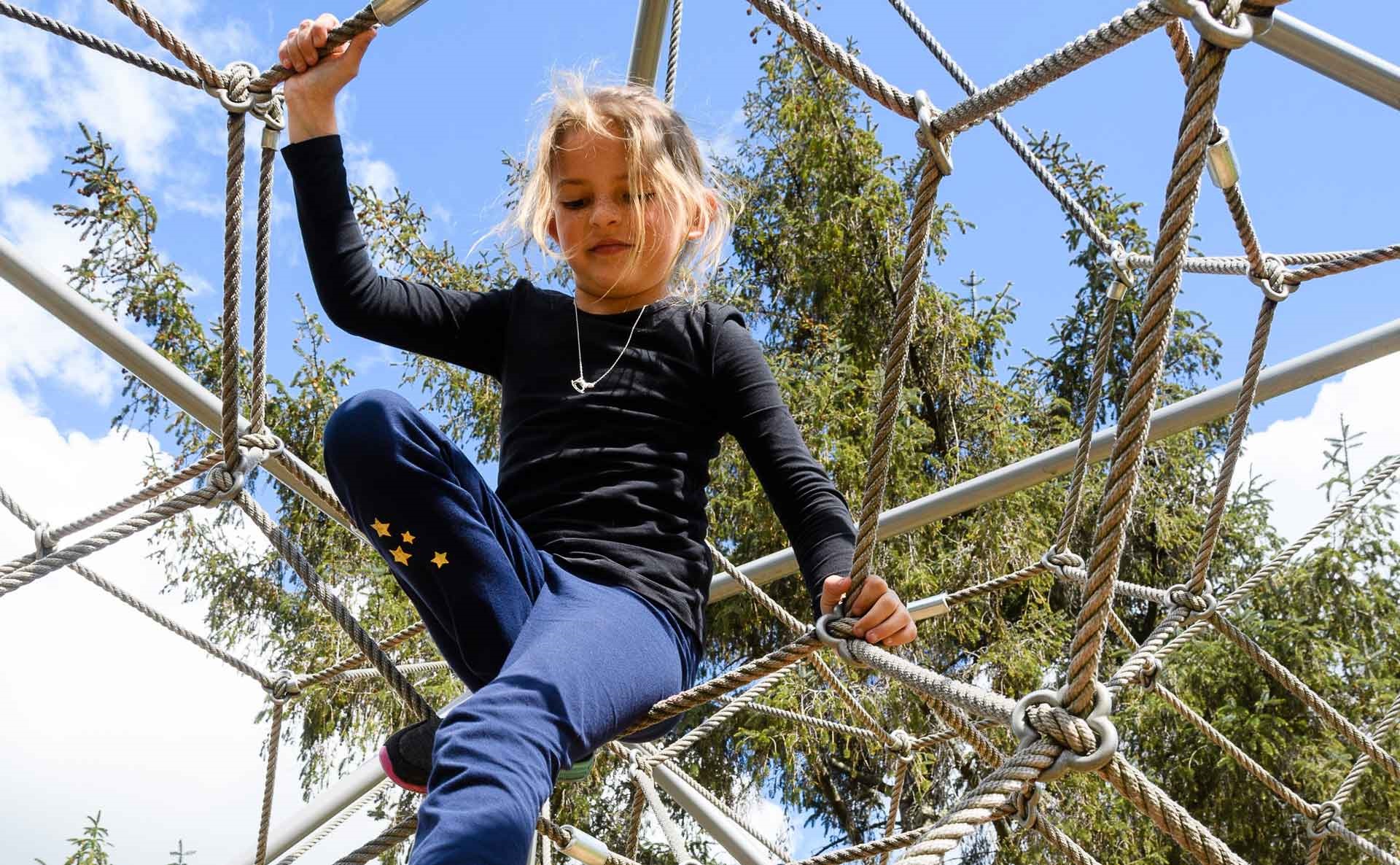 Young girl climbing on playground ropes.