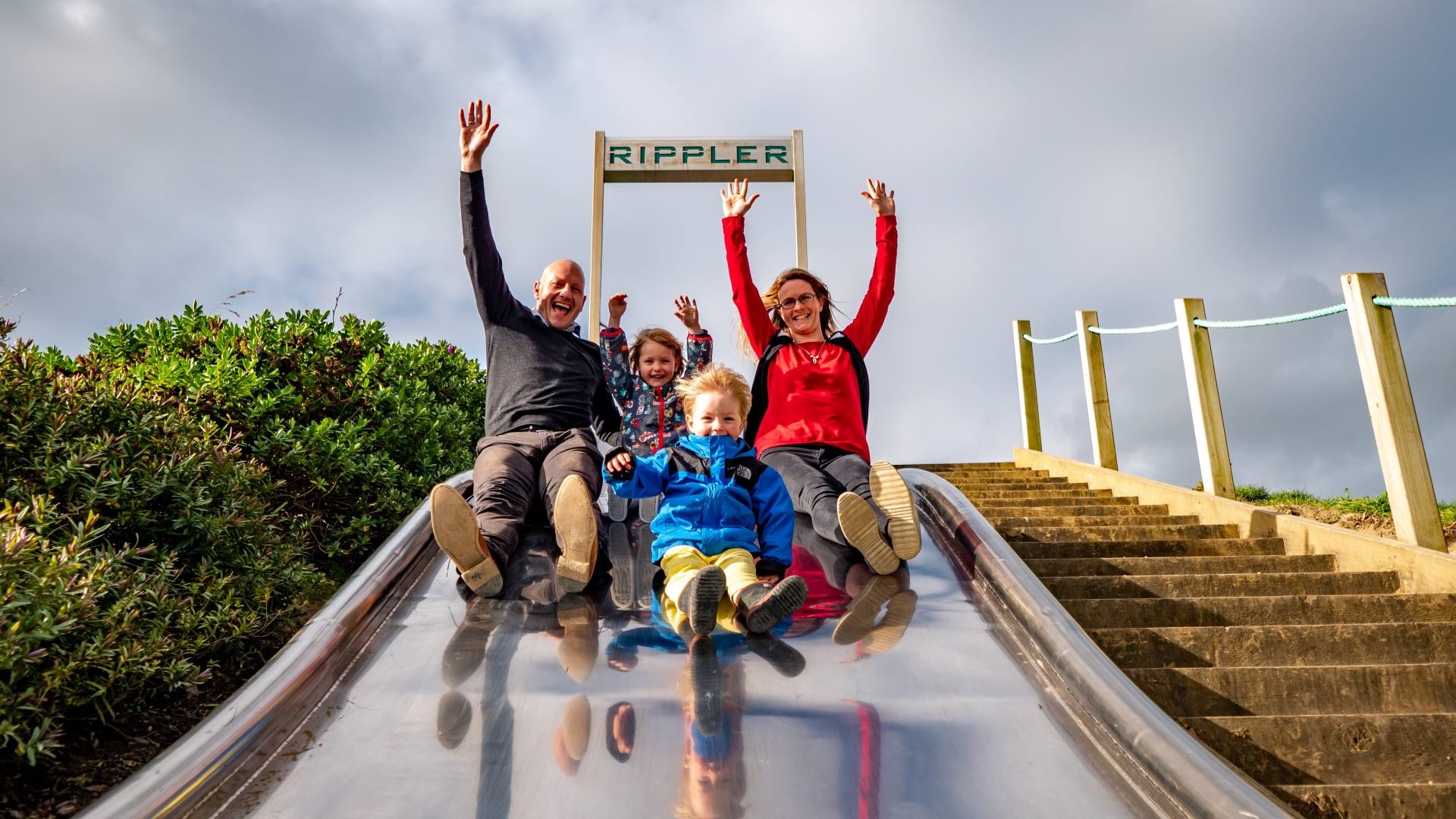 Family sliding together down a giant slide on a hill.