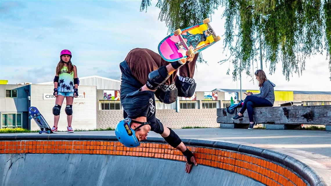 Photo shows skateboarding kid hanging upside down on the rim of the skate bowl, mid-leap.