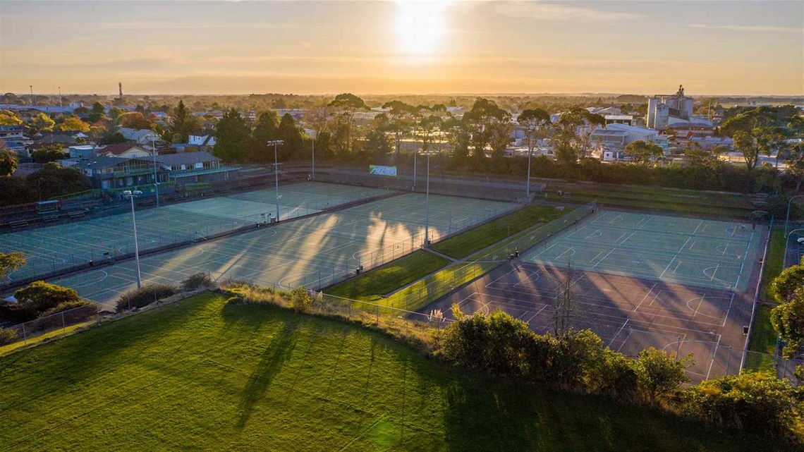 Photo shows outdoor netball courts surrounded by floodlights.