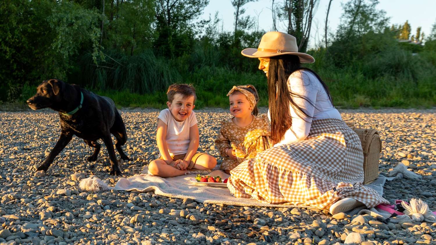 A young family picnic at the river with their dog.