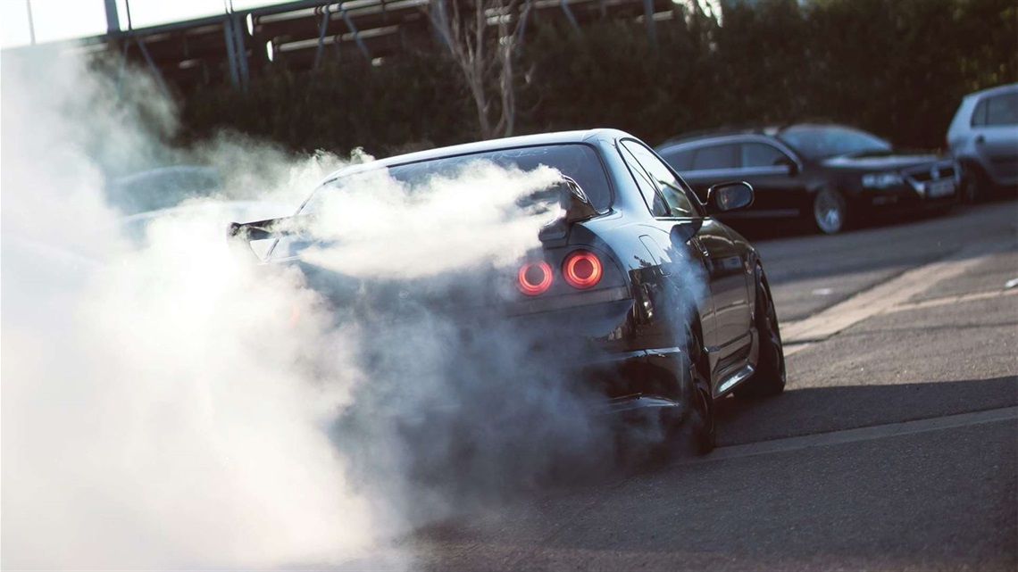 Low-slung car being driven fast and furiously along the street, with smoke streaming behind it.