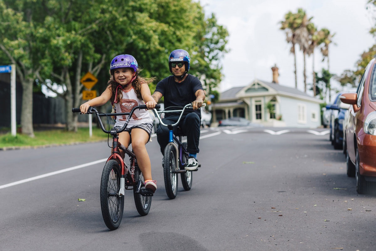 Photo shows smiling young girl and male caregiver riding bikes along a suburban street.