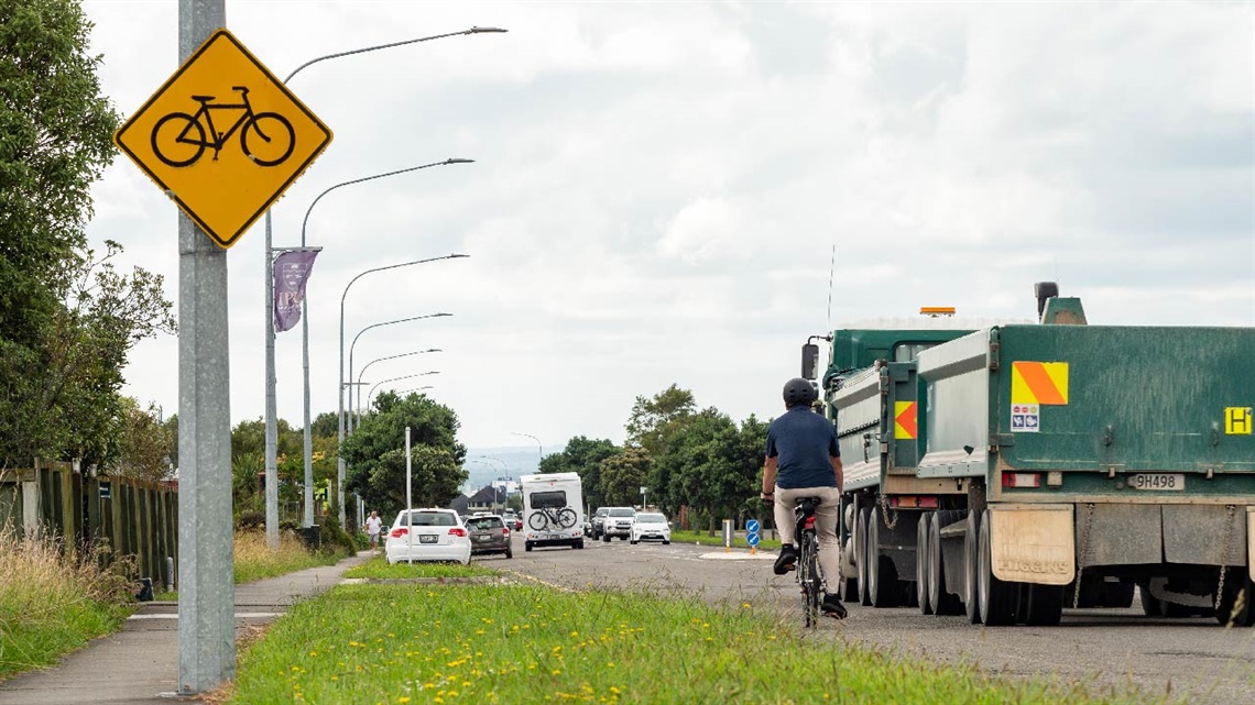 Photo shows a man cycling by a truck with a cycling road sign on the pole.