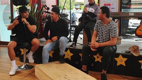 Young musicians laugh and chat on the stage inside Youth Space.