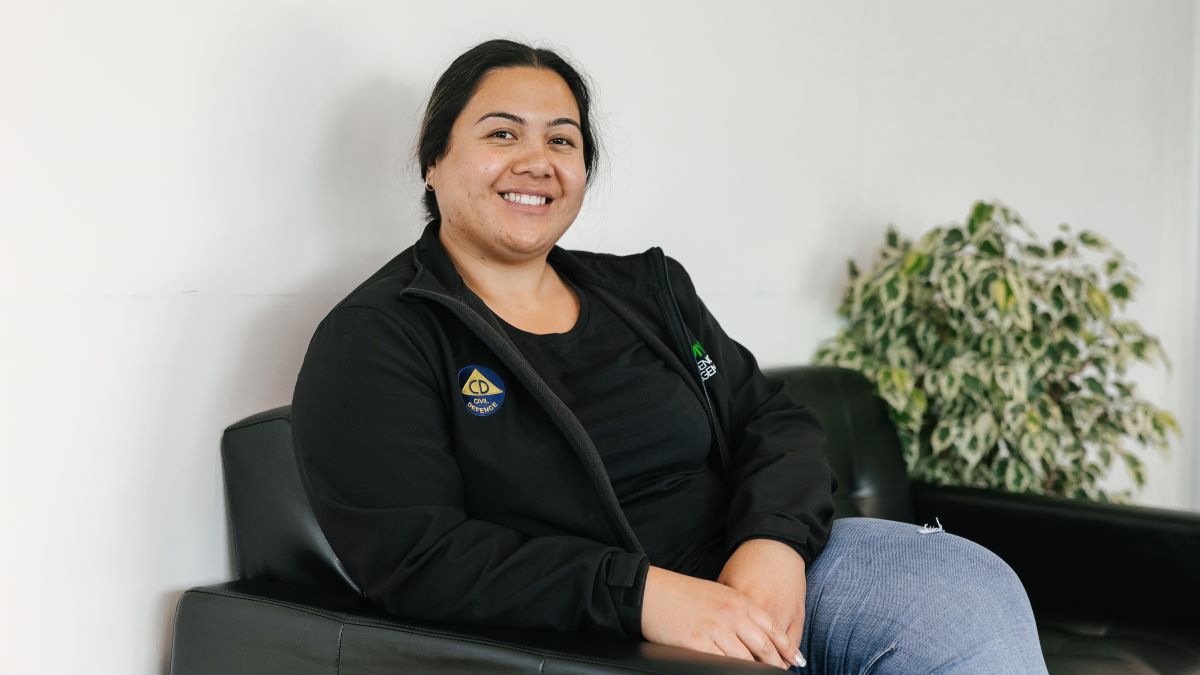 A smiling young woman sitting in an armchair with a plant behind her.