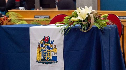 Image shows a Palmerston North city flag hanging on a blue table with flowers