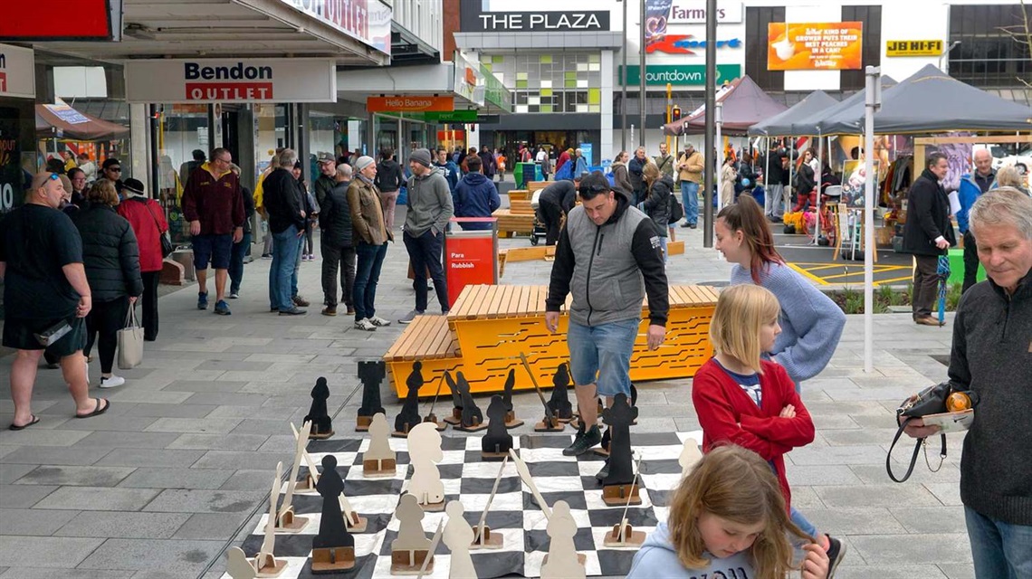 Image shows people playing giant chess on a busy street