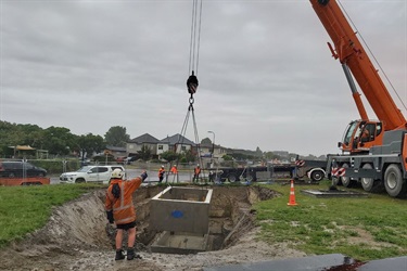 A crane lowers a concrete surround into the hole.