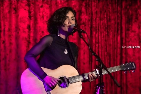 A woman singing on stage while playing the guitar