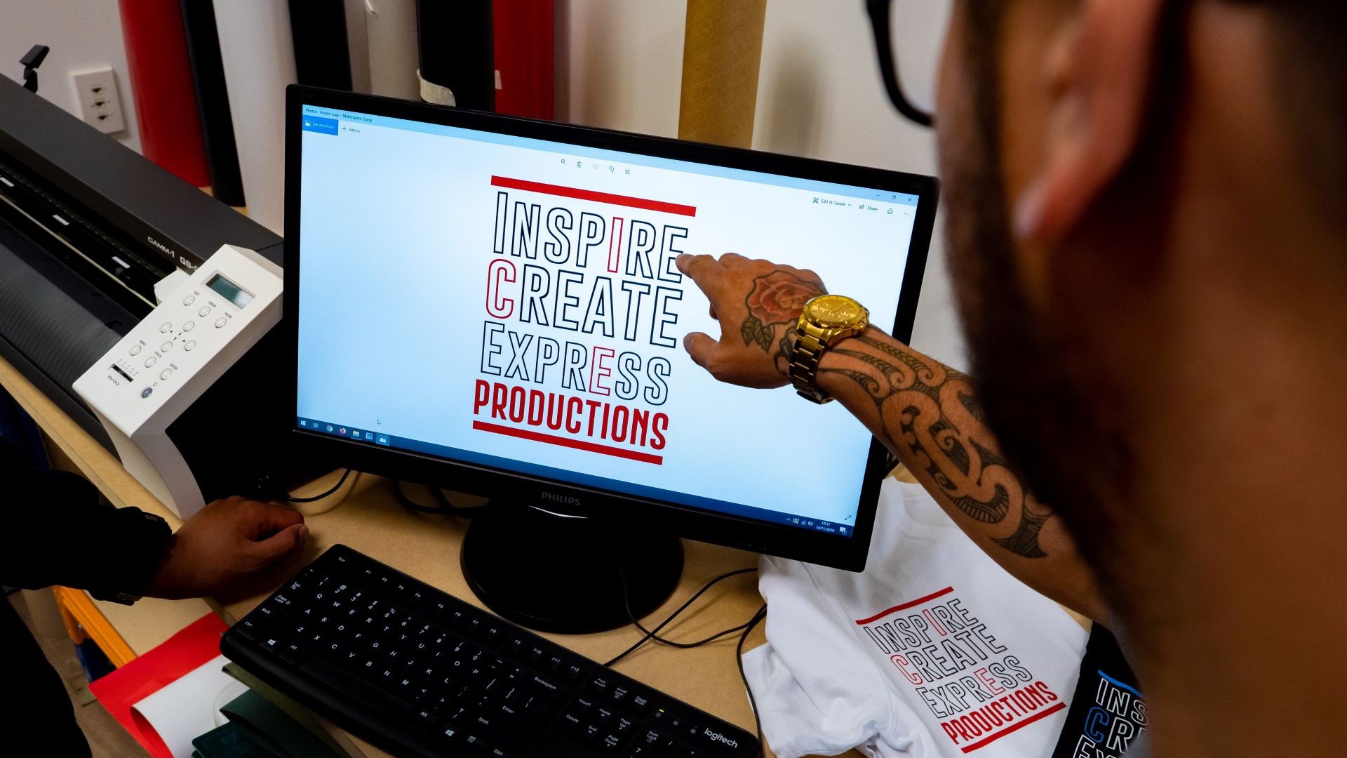 A person points to a design on a computer screen next to a t-shirt laser-printed with the same design.
