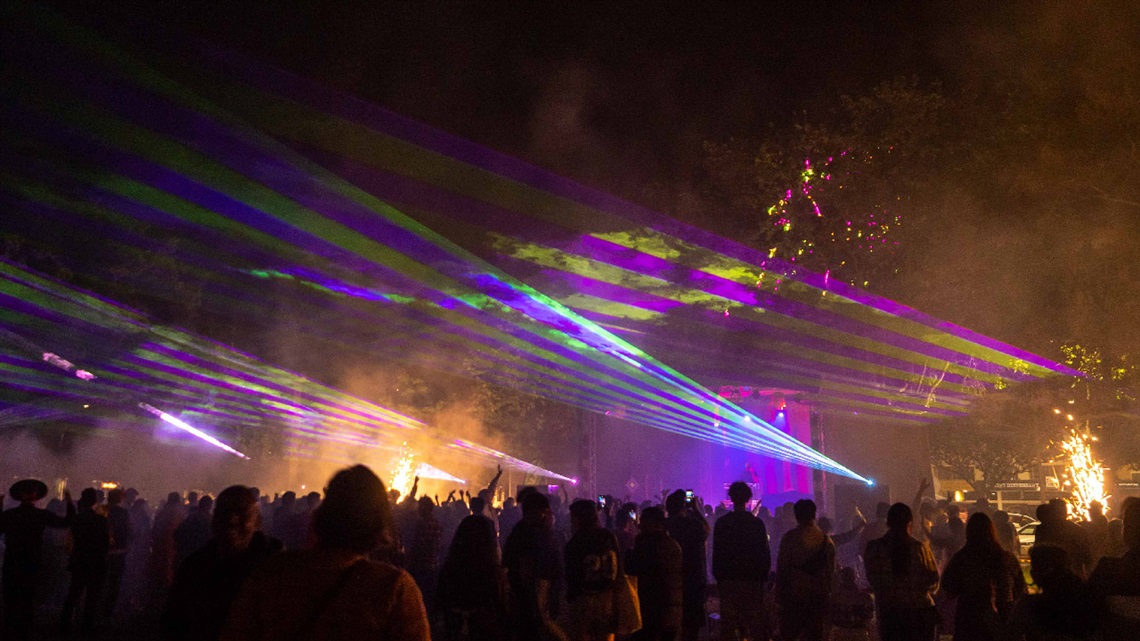 Image shows lightings in night sky with people dancing on a square