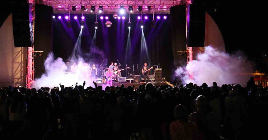 Photo shows a music band playing on stage with a large audience