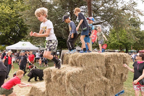 Image shows kids jumping off haystacks on a square