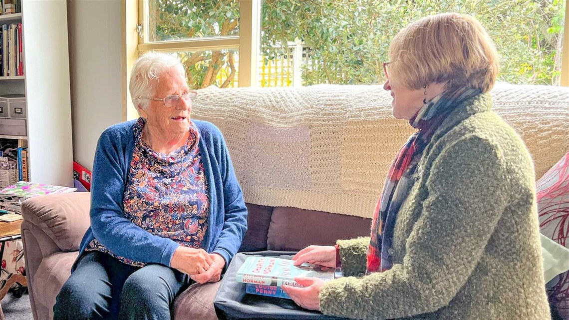 A Home Service member chats with a volunteer over a pile of books.