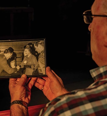 Image shows an old man looking at an old photo of the queen elizabeth