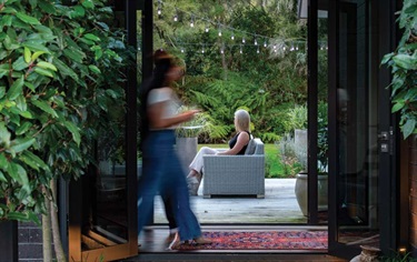 image shows a woman walking past a sliding door while another woman sitting in the courtyard