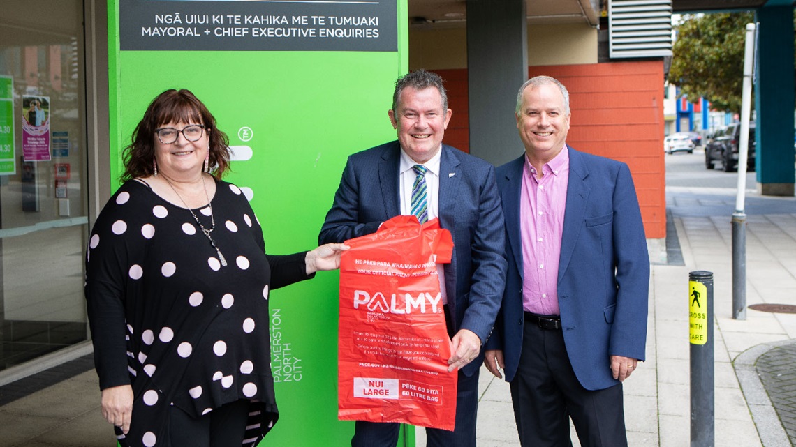 Picture shows three people standing on roadside with a red rubbish bag