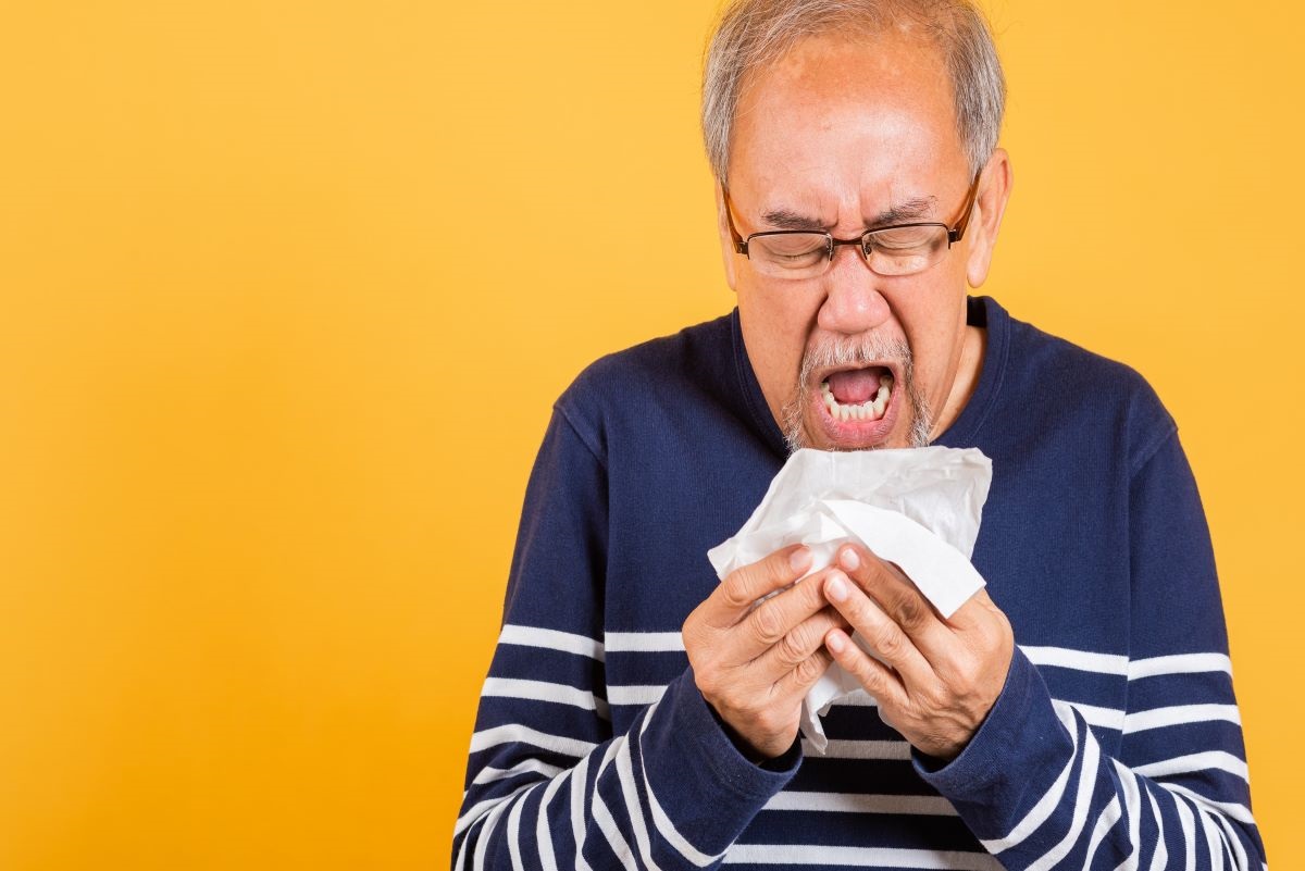Older man sneezing into a tissue.