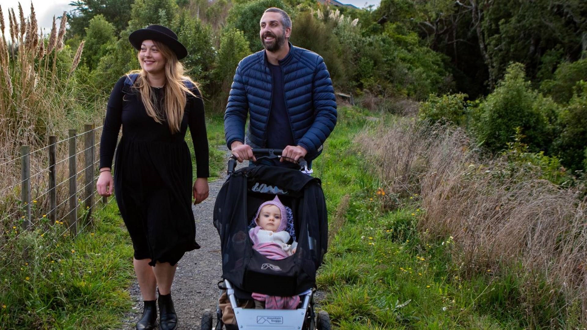 A young couple push a baby in a stroller along a scenic rural walkway.