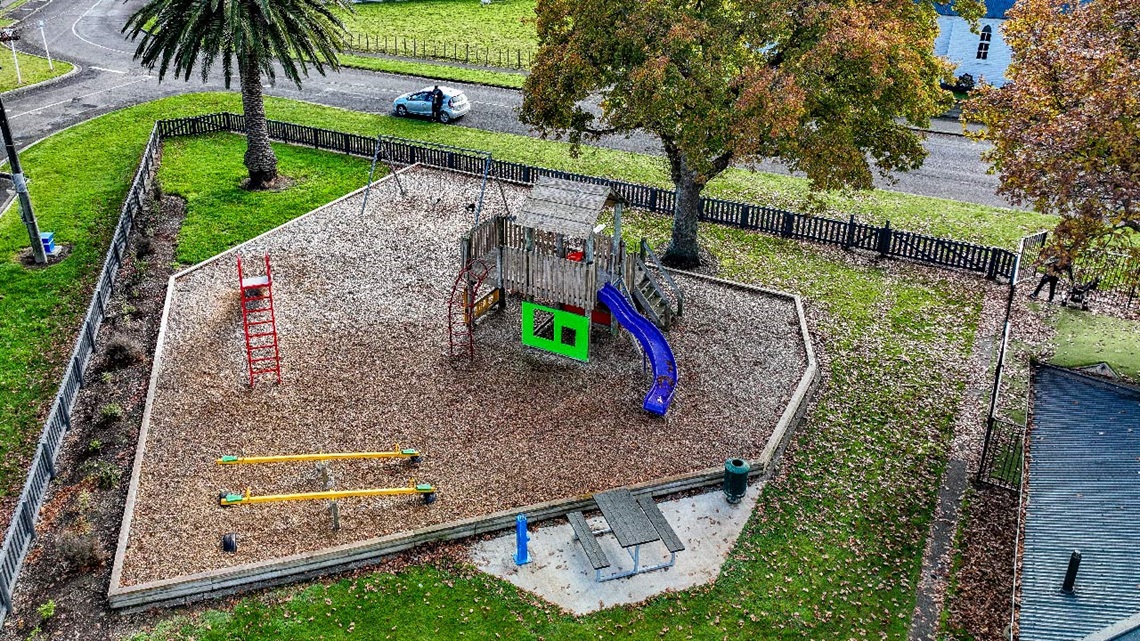 Image shows aerial view of a playground covered by mulch with dining table and drinking fountain on site.