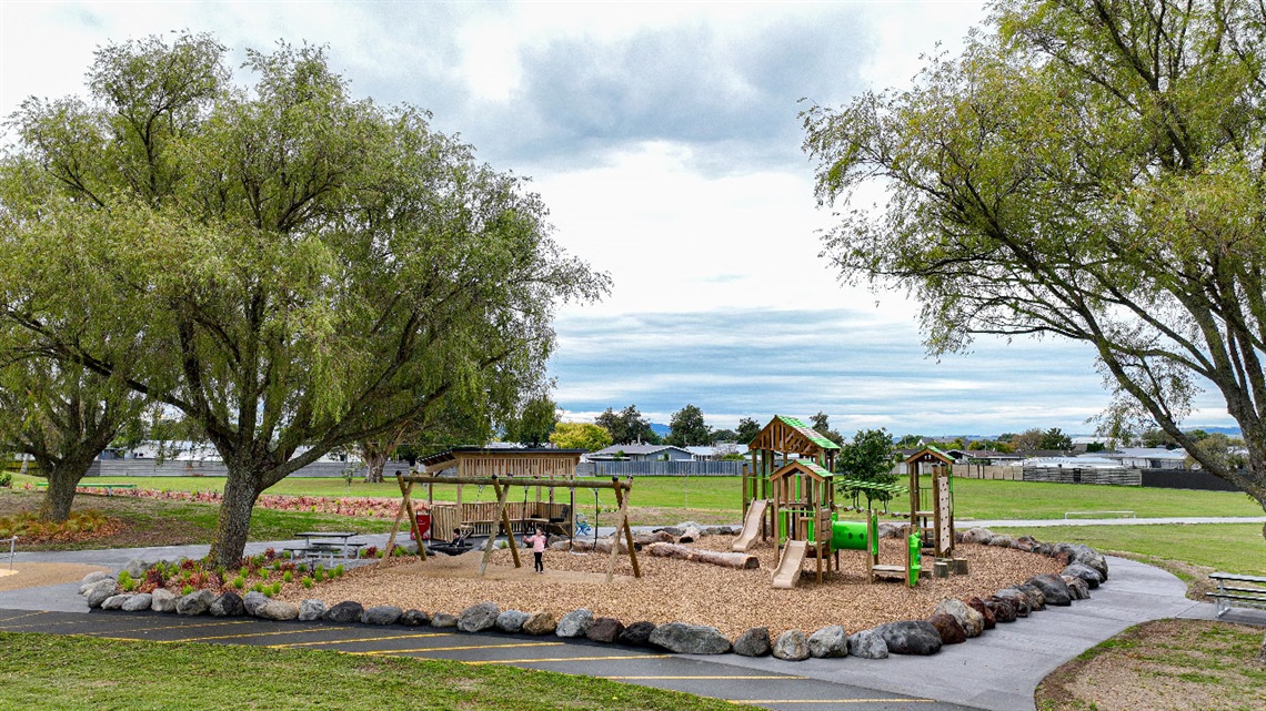 Image shows a playground surrounded by trees and walking pathway
