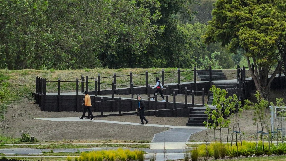 Image shows three people walking along a zigzag walkway leading to river