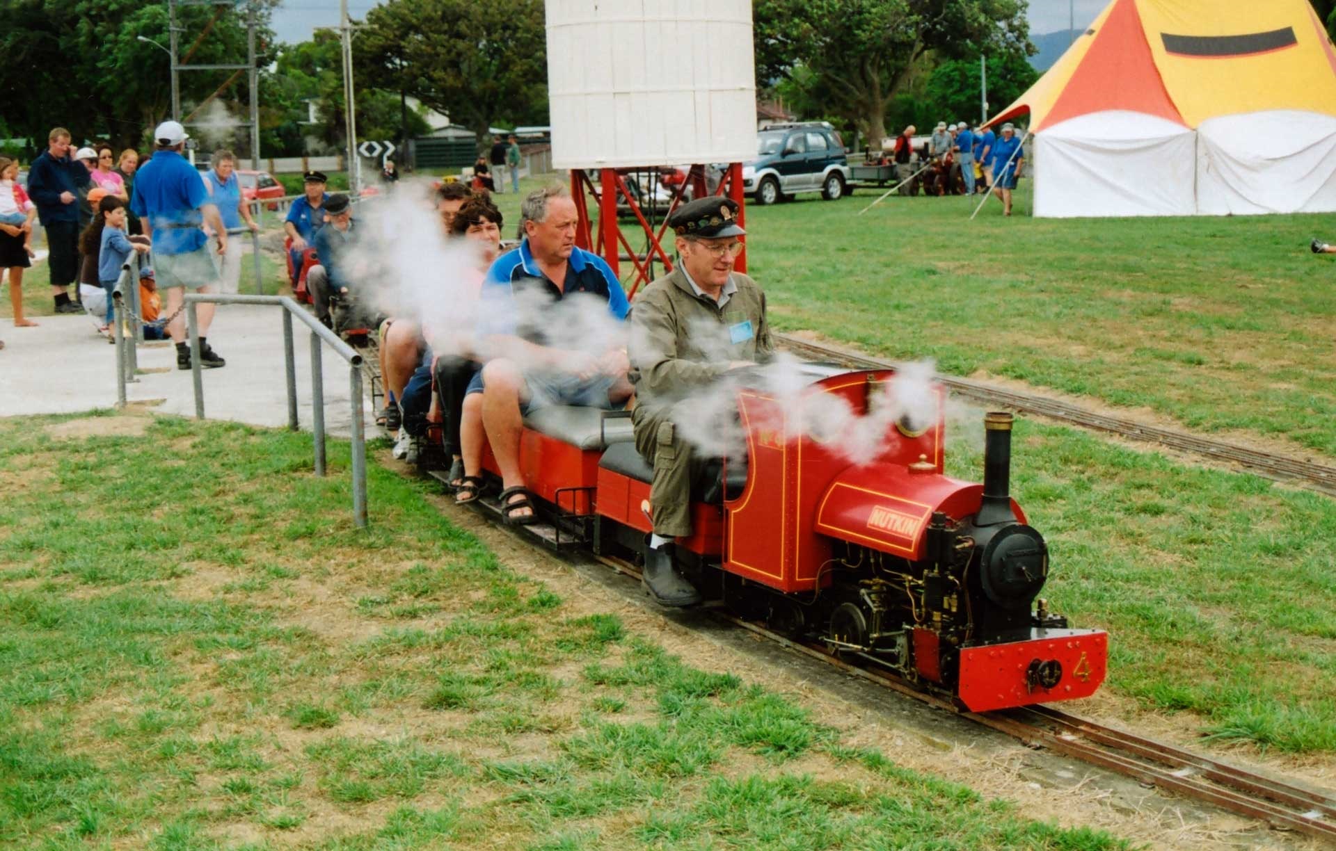 Image shows a miniature red steam train carrying people on the track.
