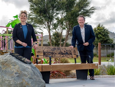 Two people stand beside a commemorative bench and plaque at Missoula Reserve during a sister city dedication event.