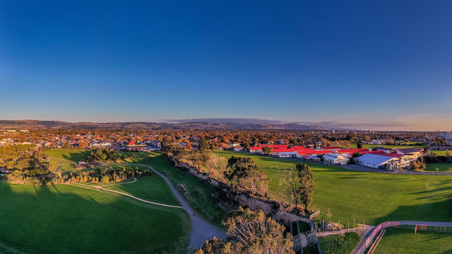 Aerial view of a walkway neighboured by a sportsfields and a small playground.