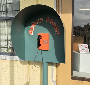 A phone on a wall outside a shop, labelled 'mystery phone'.
