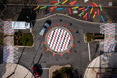 Colourful patterns painted on the ground spill over a city streetscape.