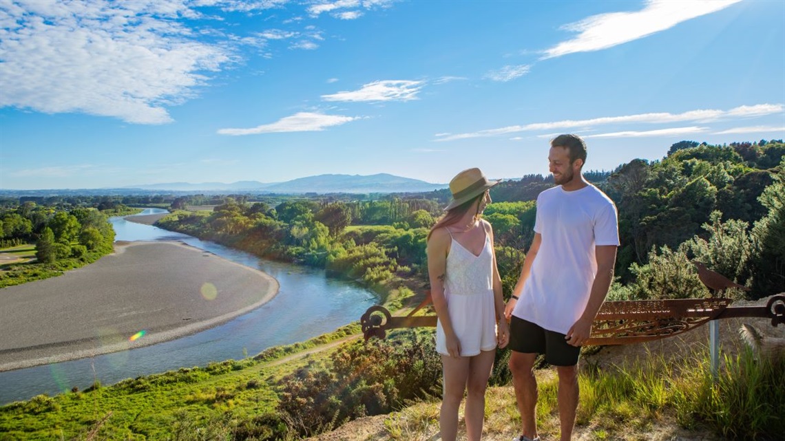 A young couple look out over the river at Te Motu o Poutoa Anzac Park, the site of our planned civic marae and cultural centre.