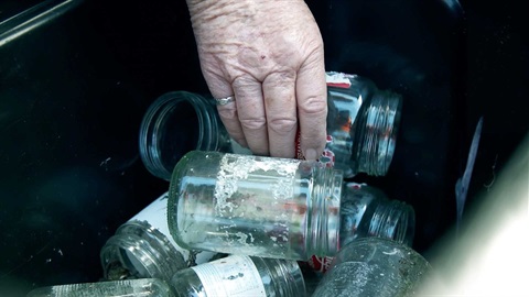 Closeup of person putting glass jars in their recycling crate.