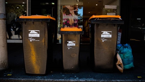 Image shows three rubbish bins and a rubbish bag on road side.