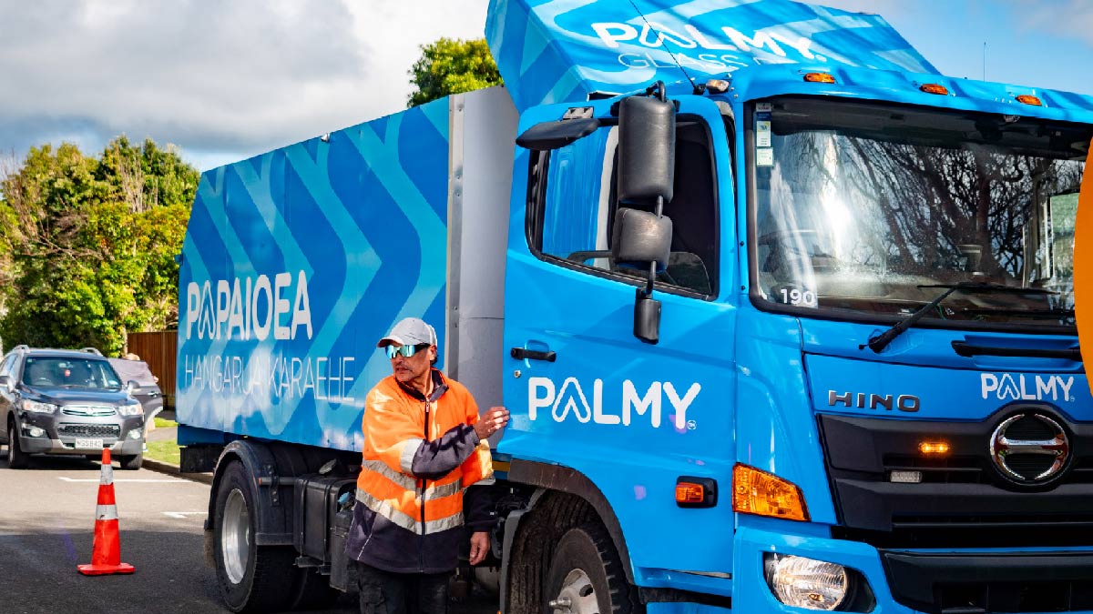 Image shows a man in high-vis jacket standing next to a blue rubbish truck