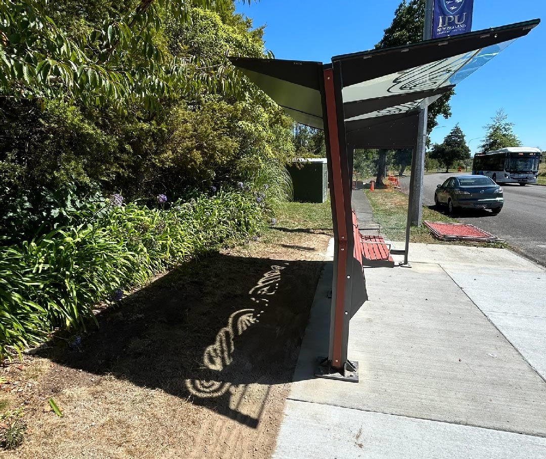 Photo shows a bus shelter under the sun, with the design on the roof also creates a shadow on the ground